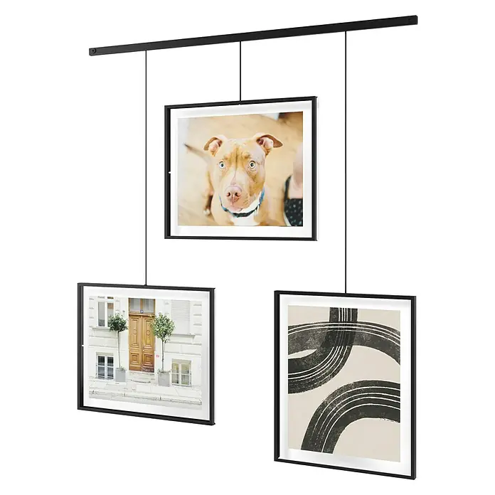 Umbra Bilderrahmen-Set Exhibit - 3 x 20x25 cm, Schwarz, Metall - Eine elegante Hängegalerie mit drei gerahmten Bildern, die von einer schwarzen Stange an der Decke abgehängt sind. Die Bilder zeigen einen Hund, eine Fassade und abstrakte Kunst.