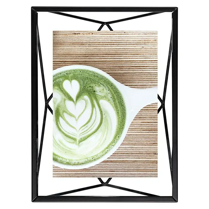Umbra Bilderrahmen Prisma - 10 x 15 cm, Schwarz, Glas - Ein gerahmtes Foto von einem Matcha Latte mit einem Herzdesign im Schaum, platziert auf einer Holzoberfläche.