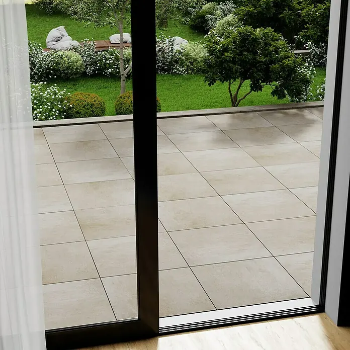 Marazzi Terrassenfliese Esterno 20T Plaster Sand - 60 x 60 x 2 cm, Sand, Matt - Ein weit geöffneter Blick durch eine Schiebetür auf eine Terrasse mit quadratischen Steinplatten und einen grünen Garten.