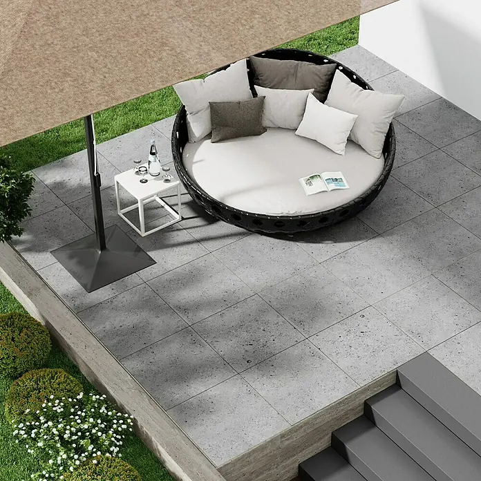 Marazzi Terrassenfliese Esterno 20T Gris Fleury - 60 x 60 x 2 cm, Grau, Matt - Ein runder Loungesessel aus Rattan mit bequemen Kissen und einer kleinen Tischgarnitur unter einem Sonnenschirm auf einer Terrasse.