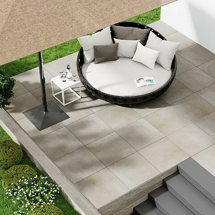 Marazzi Terrassenfliese Esterno 20T Plaster Sand - 60 x 60 x 2 cm, Sand, Matt - Rundes dunkles Rattan-Outdoor-Daybed mit hellen Kissen auf einer Terrasse.
