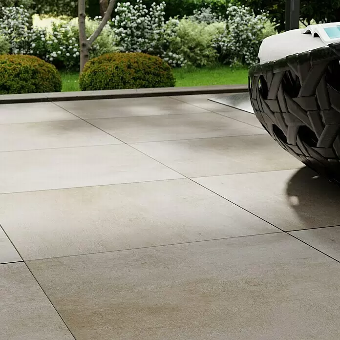 Marazzi Terrassenfliese Esterno 20T Plaster Sand - 60 x 60 x 2 cm, Sand, Matt - Helle beigefarbene Außenpflastersteine mit subtiler Textur, die einen modernen Terrassenboden neben einem Garten bilden.