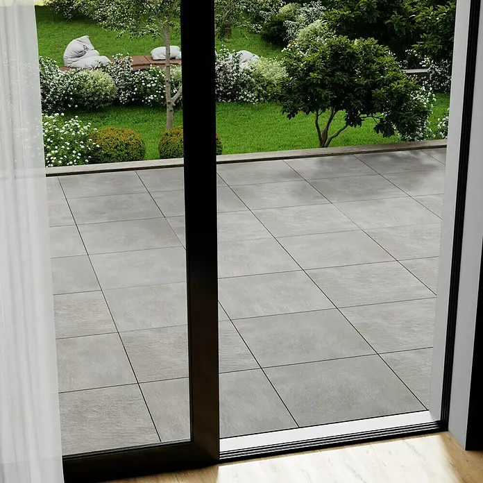 Marazzi Terrassenfliese Esterno 20T Plaster Grey - 60 x 60 x 2 cm, Grau, Matt - Blick durch eine Terrassentür auf die grauen Terrassenfliesen und den Garten.
