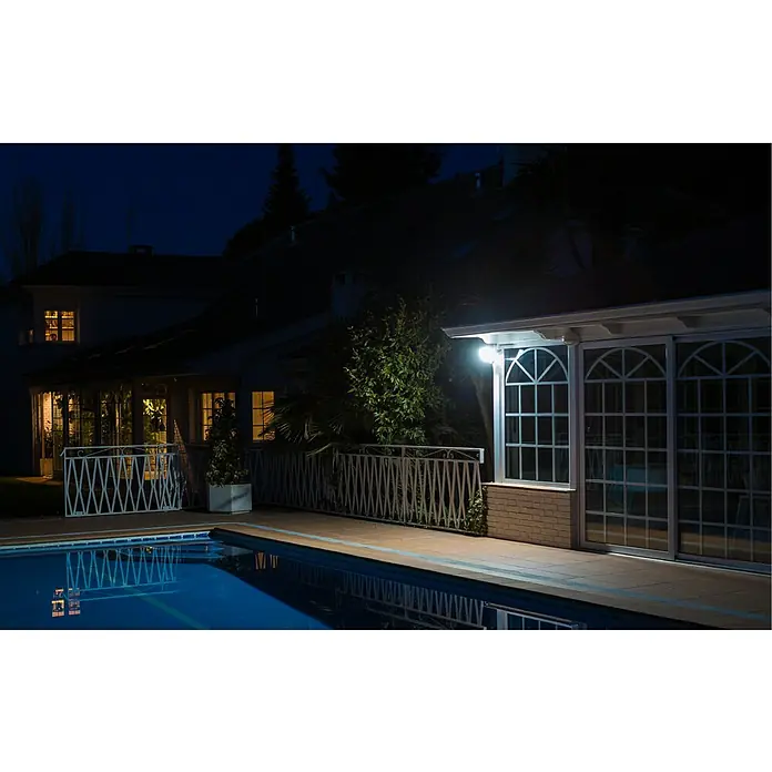 Garza Proyector LED Design - 20 W - Vista nocturna de una casa con piscina, iluminada por una luz exterior brillante que realza la arquitectura y el jardín.