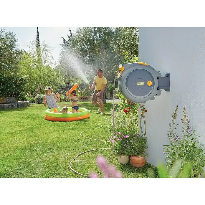 Hozelock Wand-Schlauchbox Auto Reel - Schlauchlänge: 20 m - Automatische Schlauchtrommel von Hozelock im Einsatz, während eine Familie im Garten Spaß hat.