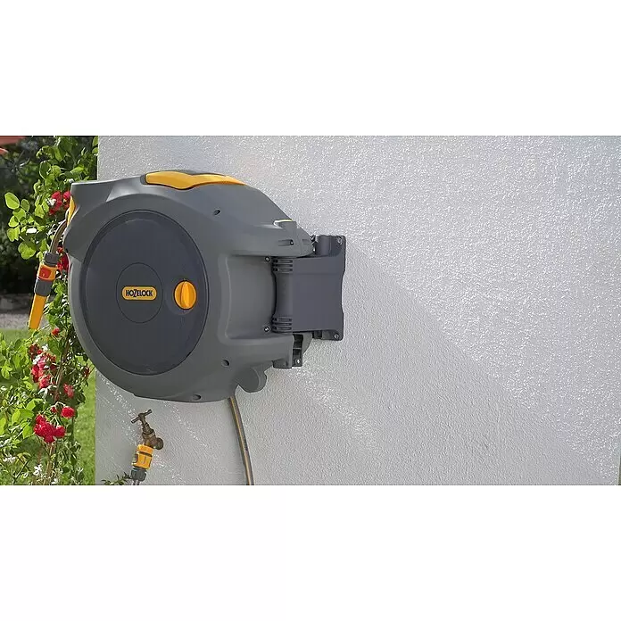 Hozelock Wand-Schlauchbox Auto Reel - Schlauchlänge: 20 m - Wandmontierte graue und gelbe Hozelock Schlauchtrommel mit Schlauch, an Wasserhahn angeschlossen, neben Rosenbusch.