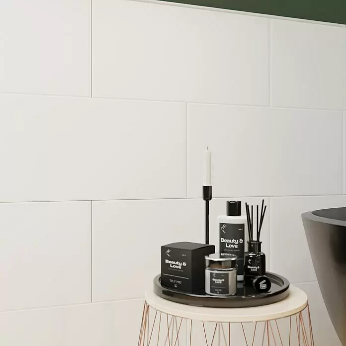 Wandfliese White Classic - 30 x 60 cm, Weiß, Matt - Beistelltisch aus Kupferdraht mit heller Platte, darauf schwarze Badezimmerprodukte: Shampoo, Lotion, Diffusor und Kerze.