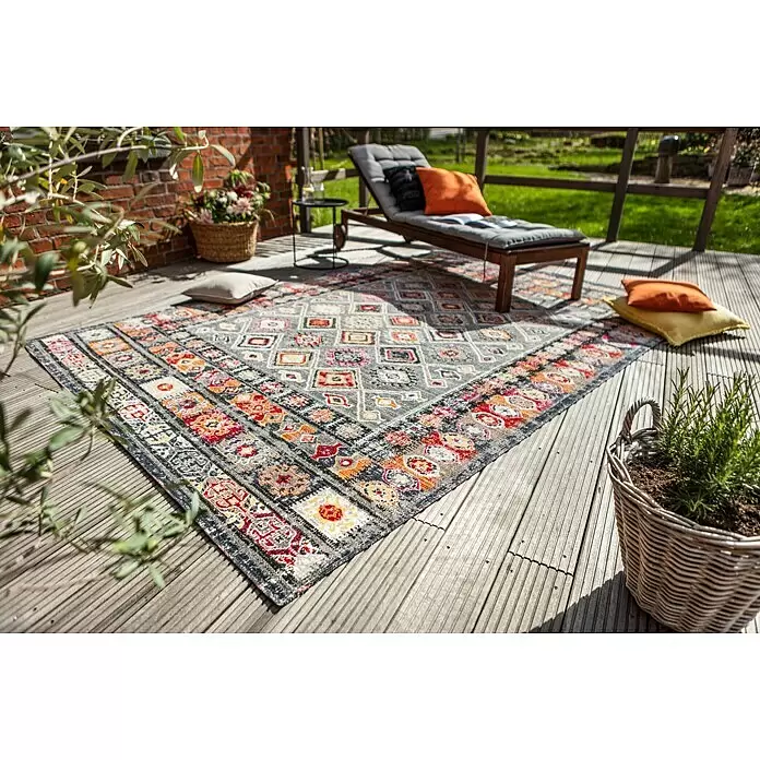Outdoor-Teppich Bonnie - Bunt Hell, 170 x 120 cm, 100 % Polypropylen - Ein bunter, aufwendig gemusterter Outdoor-Teppich auf einer Holzterrasse, der einem gemütlichen Sitzbereich Wärme verleiht.