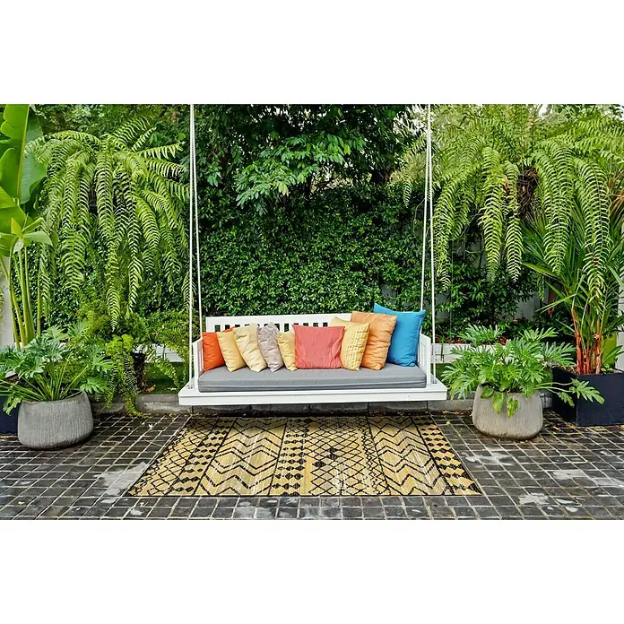 Outdoor-Teppich Bonnie - Gelb, 170 x 120 cm, 100 % Polypropylen - Einladende Hollywoodschaukel mit bunten Kissen auf einem gemusterten Teppich, umgeben von üppigem Grün, die zum Entspannen im Garten einlädt.