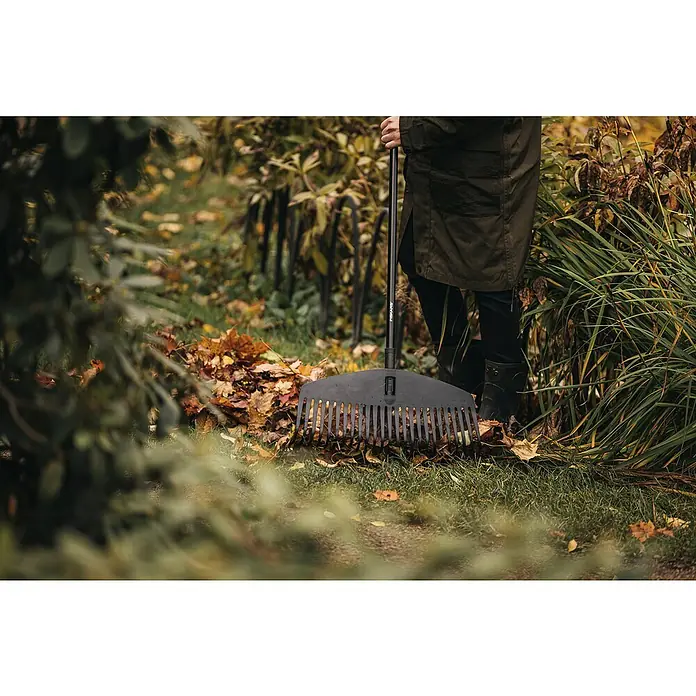 Fiskars Solid Laubbesen - Arbeitsbreite: 52 cm, Anzahl Zinken: 24, Art Stiel: Langstiel - Eine Person benutzt einen Fiskars Rechen im Garten, um herabgefallenes Laub zu sammeln.