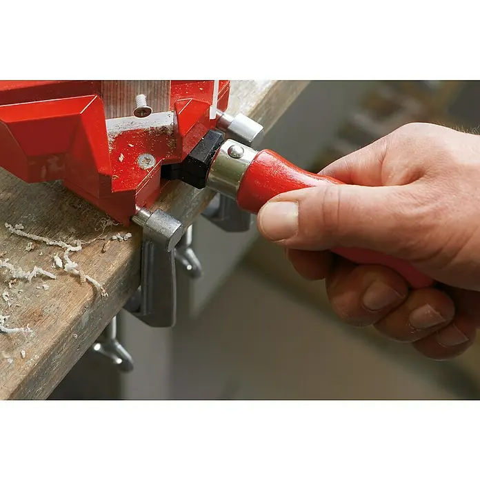 Bessey Tischklemme TK 6Spannweite: 60 mm - Bild einer Hand, die eine Eckspannzwinge mit einem roten Griff festzieht, um zwei Holzstücke in einem 90-Grad-Winkel zu fixieren.