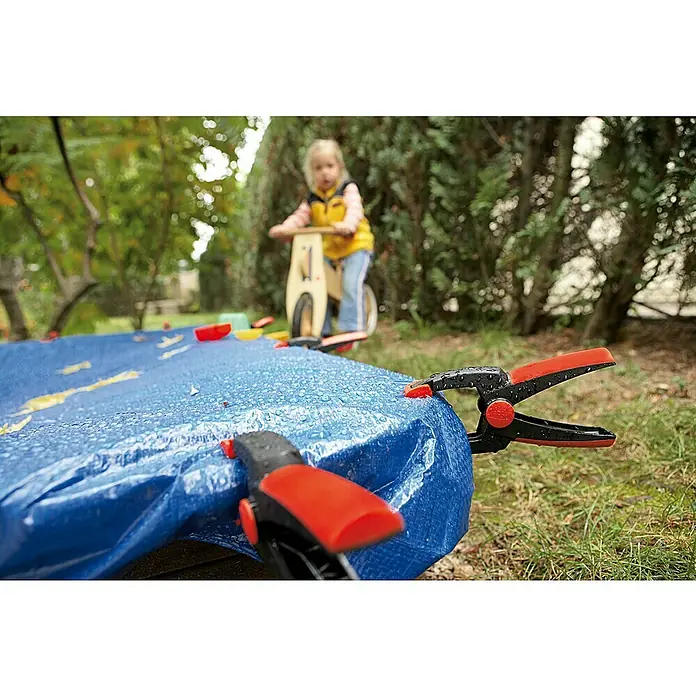 Bessey Federzwinge Clippix XC 2 - Spannweite: 25 mm, Spannkraft: 40 N, Ausladung: 30 mm - Nahaufnahme von zwei wetterfesten Planen-Klammern mit rotem Griff, die eine blaue Plane sichern, ideal für den Einsatz im Freien.