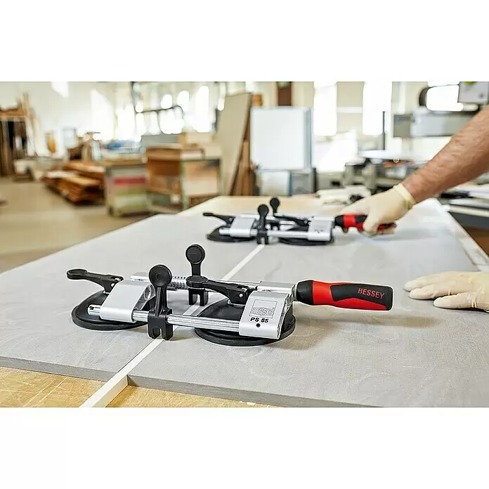 Bessey PS 55 -  - Zwei Bessey PS 55 Nahtspanner, silber mit rot/schwarzen Griffen, verbinden zwei hellgraue Werkstücke. Eine behandschuhte Hand justiert ein Werkzeug.