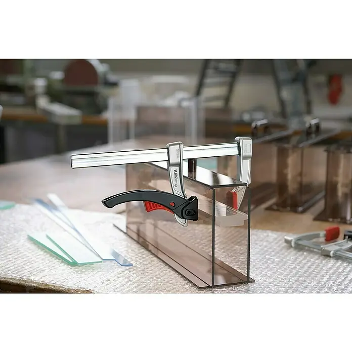Bessey Hebelzwinge KliKlamp KLI 16 - Spannweite: 160 mm, Spannkraft: 1.200 N, Ausladung: 80 mm - Eine KliKlamp-Stange ist an einer Kunststoffbox befestigt, die das Kleben des Materials während des Herstellungsprozesses unterstützt.