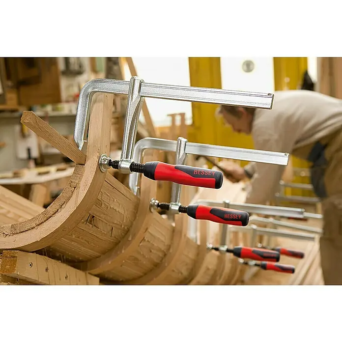 Bessey Schraubzwinge GZ20B10 - Spannweite: 200 mm, Spannkraft: 6.000 N, Ausladung: 100 mm - Blick auf eine Holzkonstruktion, die mit mehreren BESSEY Schraubzwingen fixiert ist, im Hintergrund arbeitet eine Person.