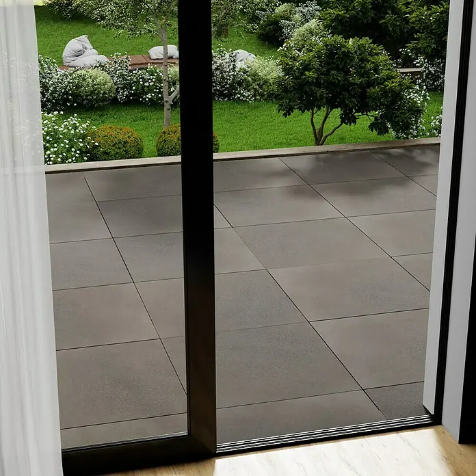 Marazzi Terrassenfliese Esterno 20T Material80 x 80 x 2 cm, Grau, Matt - Blick durch eine geöffnete Terrassentür auf graue Terrassenfliesen und einen gepflegten Garten. Helle Vorhänge links.