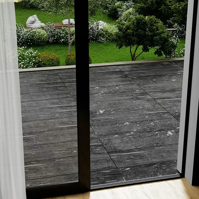 Marazzi Terrassenfliese Esterno 20T Davos - 40 x 120 x 2 cm, Anthrazit, Matt - Blick durch eine offene Terrassentür auf graue Terrassenplatten und einen grünen Garten mit üppiger Bepflanzung und Sitzgelegenheiten.