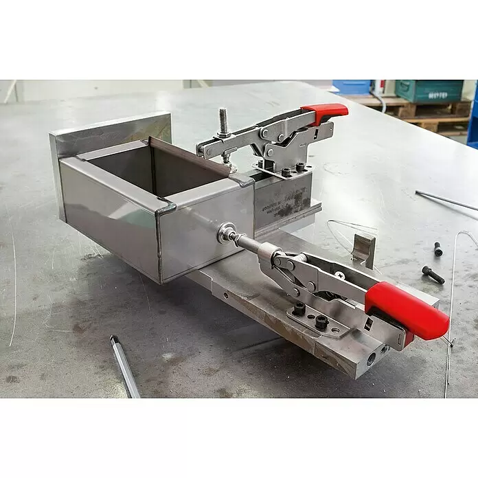 Bessey Schnellspanner STC-IHH25 - Spannweite: 16 mm, Spannkraft: 2.500 N - Edelstahl-Schweißvorrichtung mit zwei rotgriffigen Spannverschlüssen hält ein rechteckiges Metallwerkstück.