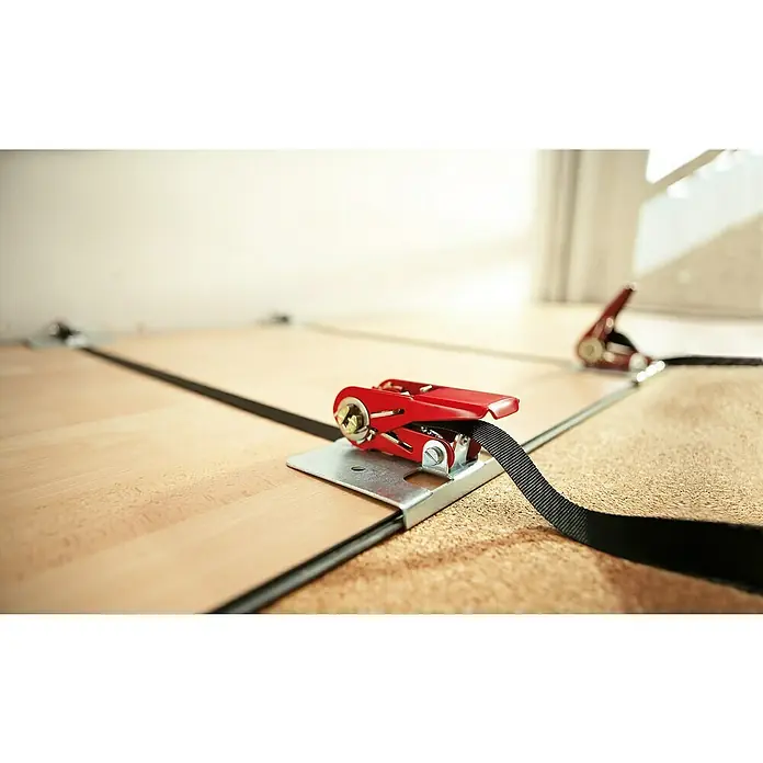 Bessey Parkett-Verlege-Hilfe SVH 400 - Spannweite: 4 m - Nahaufnahme eines roten Spanngurtes mit schwarzem Gurtband auf hellbraunem Untergrund, der zur Ladungssicherung dient.