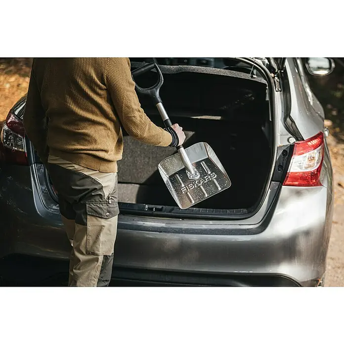 Fiskars Solid Autoschaufel - Breite: 25,5 cm, Aluminium, Geeignet für: Schnee - Eine Person verstaut eine Fiskars Schneeschaufel mit Aluminiumblatt im Kofferraum eines Autos.