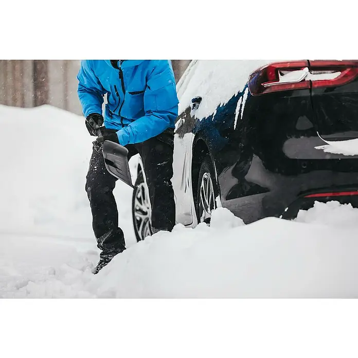 Fiskars Solid Autoschaufel - Breite: 21,5 cm, Kunststoff, Geeignet für: Schnee - Eine Person schaufelt mit einem Schneeschieber Schnee um ein schwarzes Auto herum, um es freizulegen.