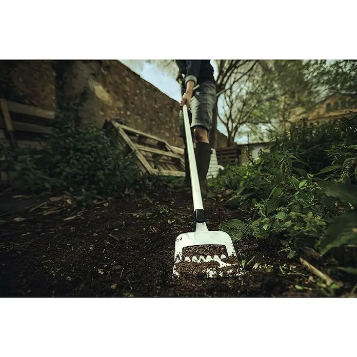 Fiskars Xact Jäter - Arbeitsbreite: 13,5 cm, Gezahntes Blatt - Nahaufnahme eines weißen Gartenrechen, der im Garten in die Erde gesteckt wird. Perfekt für die Gartenarbeit und die Vorbereitung des Bodens.