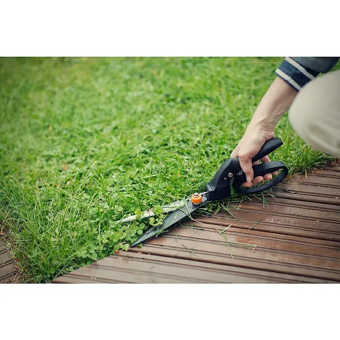 Fiskars Smartfit Rasenkantenschere GS40 - Länge: 35,5 cm - Gras wird mit einer Grasschere getrimmt, um einen sauberen Rasenrand zu erhalten. Die Schere liegt auf einer Holzterrasse.