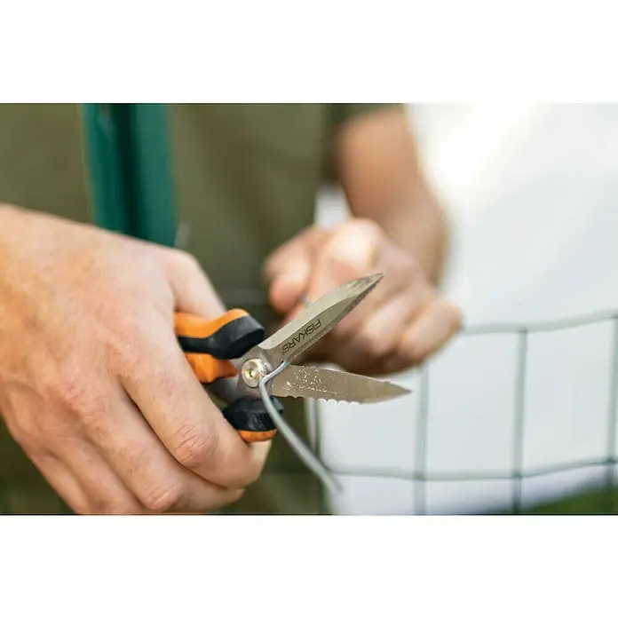 Fiskars Solid Mehrzweck-Schere SP320 - Länge: 20,6 cm - Nahaufnahme einer Person, die mit einer Fiskars-Gartenschere ein Stück Draht schneidet, wobei der Fokus auf der orangefarbenen Schere liegt.