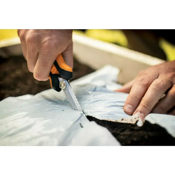 Fiskars Solid Mehrzweck-Schere SP320 - Länge: 20,6 cm - Detailaufnahme einer Hand, die mit einer Gartenschere eine weiße Plastikfolie schneidet, vermutlich für Gartenarbeiten.