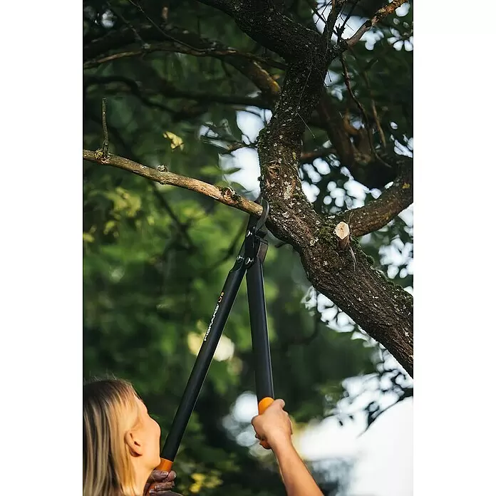 Fiskars Hand-Astschere PowerGear II L78 - Länge: 69,2 cm, Max. Aststärke: 50 mm, Stahl, Orange/Schwarz - Eine Person schneidet mit einer schwarz-orangen Fiskars L70 Astschere einen Ast.