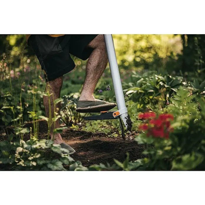 Fiskars Xact Hand-Blumenzwiebelpflanzer - Länge: 105 cm - Nahaufnahme eines Mannes, der im Garten arbeitet und mit einem Fiskars Unkrautstecher Unkraut entfernt. Fokus auf dem Werkzeug und dem Gärtner.