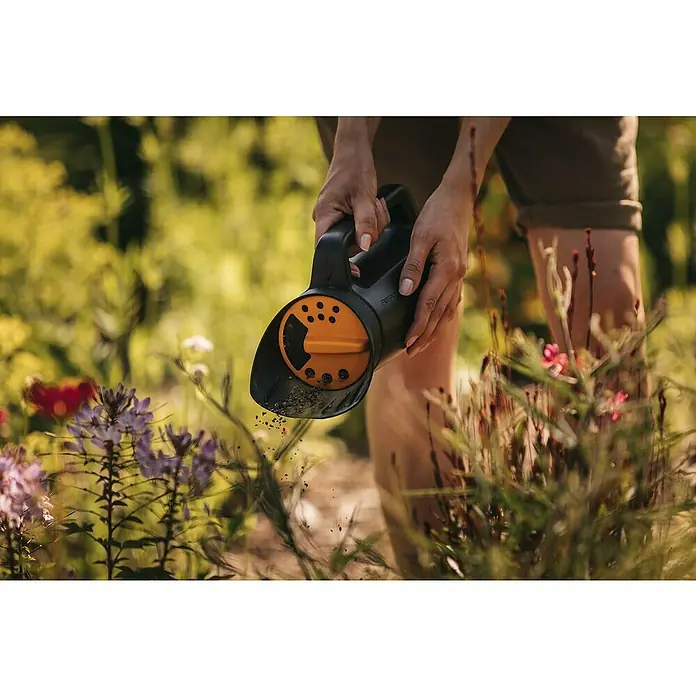 Fiskars Solid Handstreuer - 2 l - Gärtner mit einem Fiskars-Streuwagen, der im Garten Samen auf eine Blumenfläche ausbringt.