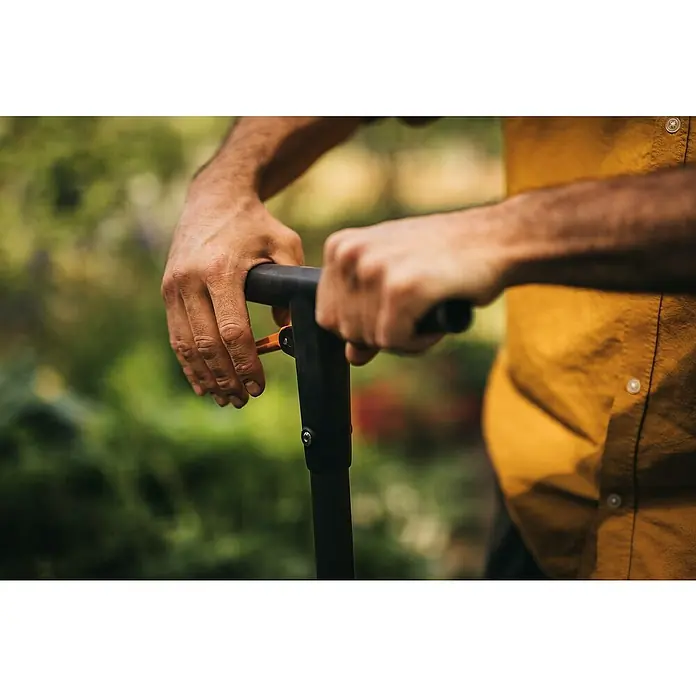 Fiskars Hand-Blumenzwiebelpflanzer - Länge: 100 cm - Nahaufnahme von Händen, die einen höhenverstellbaren Spaten bedienen, ideal für komfortables und ergonomisches Gärtnern im Freien.