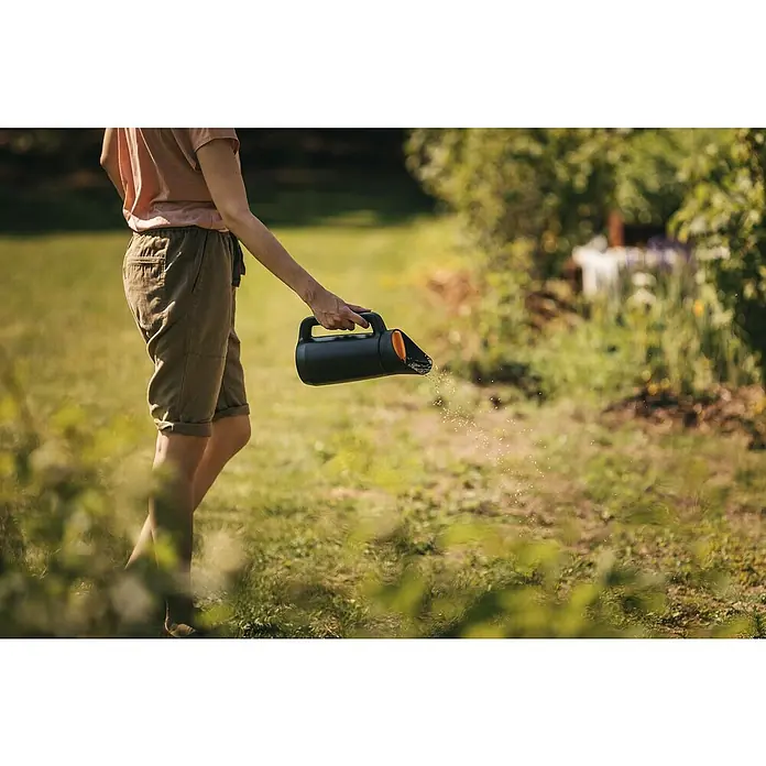 Fiskars Solid Handstreuer - 2 l - Frau gießt mit einer schwarzen Gießkanne mit orangem Ausguss Pflanzen im Garten.