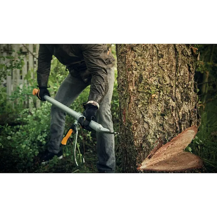 Fiskars WoodXpert Fällheber mit Wendehilfe M - 70 cm - Ein Mann benutzt eine Fiskars Astsäge mit Stiel, um einen Baum zu sägen, wobei der Fokus auf der Säge und dem Baum liegt.