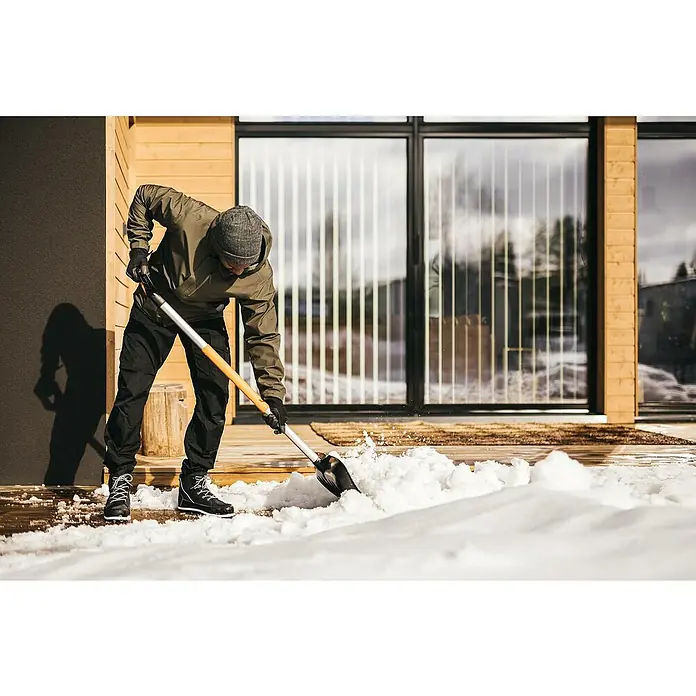 Fiskars X-series Schneeschieber mit Aufbug - Breite: 53 cm - Ein Mann schaufelt Schnee vor einem modernen Haus. Der Fokus liegt auf der Schneeschaufel und der Bewegung des Schnees.