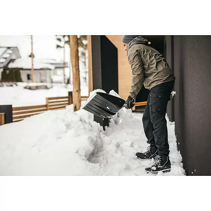 Fiskars X-series Schneeschaufel - Breite: 36 cm - Person schaufelt Schnee mit einer schwarz-orangen Schneeschaufel.