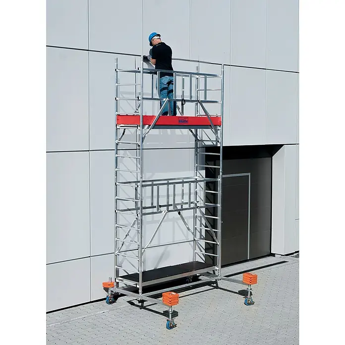 Krause ProTec Rollgerüst - Arbeitshöhe: 5,3 m, Belastbarkeit Plattform: 240 kg - Mann auf einem Krause Fahrgerüst vor einer hellen Fassade bei Inspektionsarbeiten. Das Gerüst hat orangefarbene Details und blaue Räder.