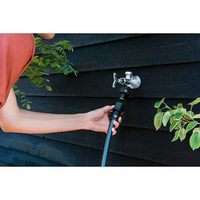 Fiskars FiberComp Hahnverbinder Multi - Multigewinde, 21 mm (G ½″) - Person verbindet schwarzen und blauen Gartenschlauch-Anschluss an silbernen Wasserhahn an dunkler Holzwand.