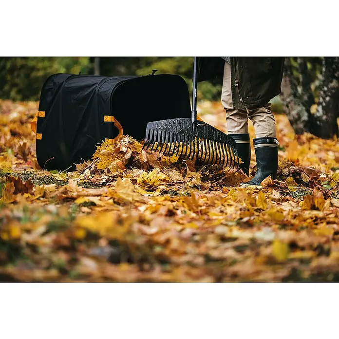 Fiskars Ergo Pop-Up Gartenabfallsack - 219 l - Nahaufnahme eines Fiskars-Laubrechens beim Aufsammeln von Herbstlaub, mit einem Laubsack im Hintergrund.