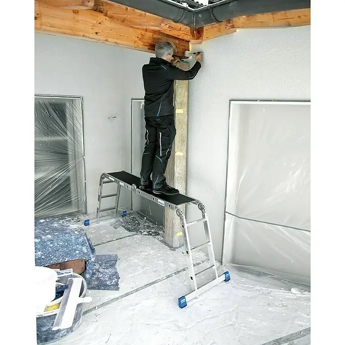Krause Combi Multiboard für Gelenkleitern - Länge: 81 cm - Ein Mann steht auf einer Krausse Arbeitsbühne und arbeitet an der Decke. Die Bühne ist stabil und sicher für Arbeiten in der Höhe.