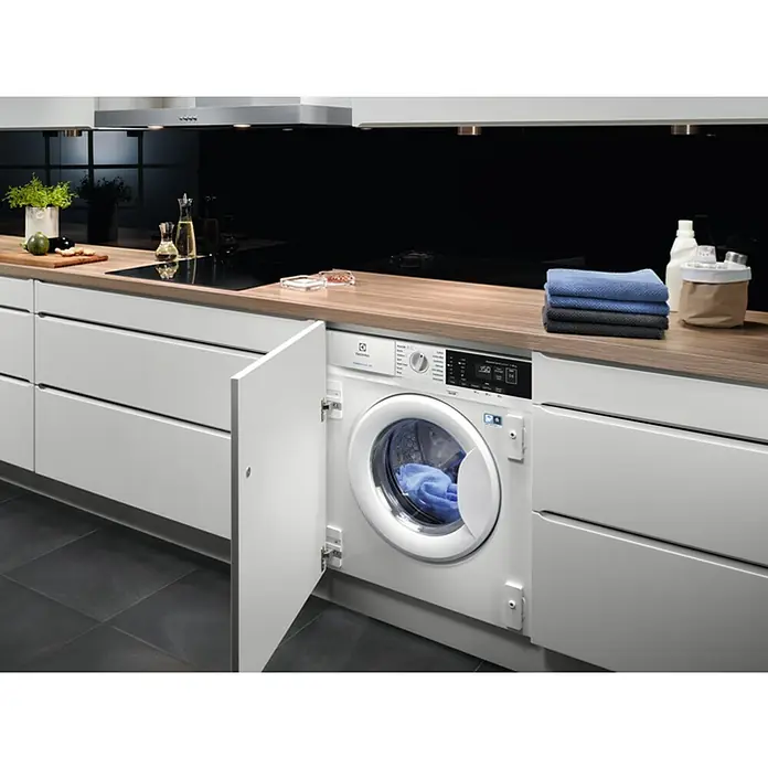 AEG Lavadora EN7F4722AN - L x An x Al: 55,3 x 59,6 x 81,9 cm, 7 kg, Potencia máx.: 2.200 W - Lavadora integrable Electrolux con puerta abierta, integrada en muebles de cocina modernos, ofreciendo funcionalidad y diseño elegante.