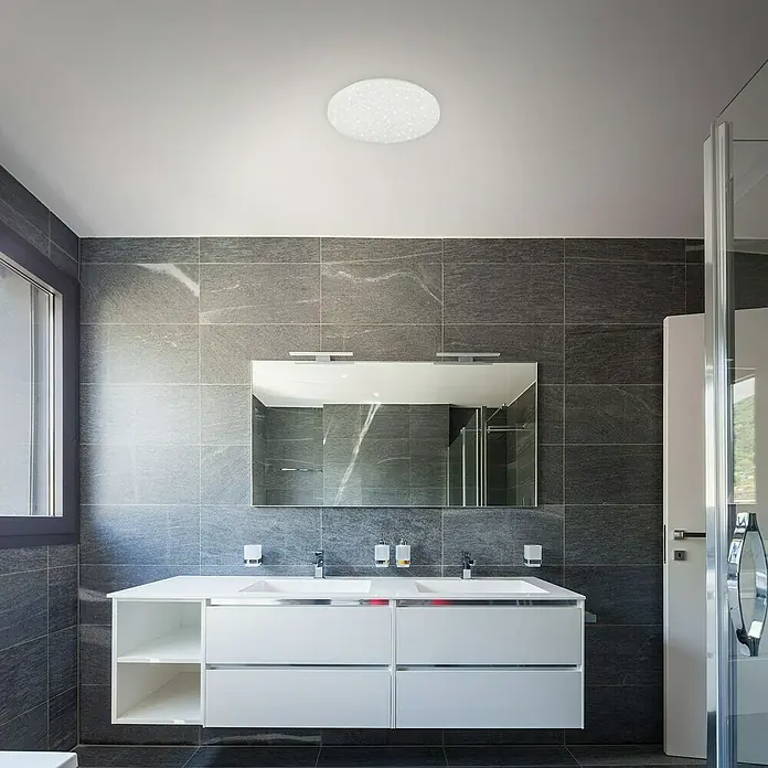 Briloner Plafón LED redondo Brili - Ø x Al: 38,5 x 7,5 cm, Blanco, Blanco neutro - Un baño moderno con una lámpara de techo redonda que ilumina la habitación. La habitación tiene azulejos grises y un mueble de baño blanco.