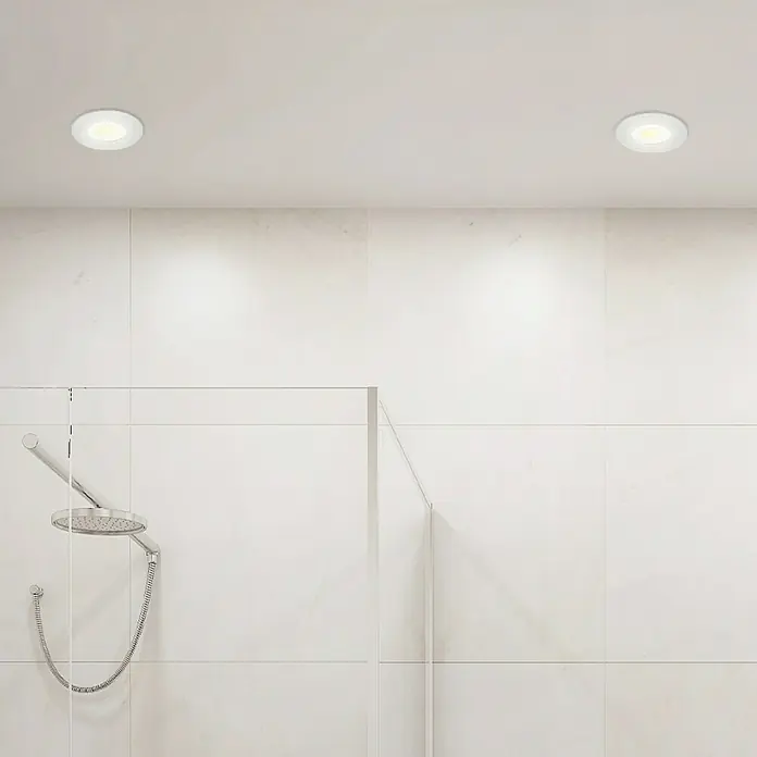 Briloner Set de focos LED empotrables redondos Kulana - 20 W, Ø x Al: 9 x 2,5 cm, 4 ud., Blanco cálido, Blanco - Dos luces LED empotradas en el techo iluminan un baño moderno con azulejos blancos y una mampara de ducha de cristal, creando un ambiente luminoso.