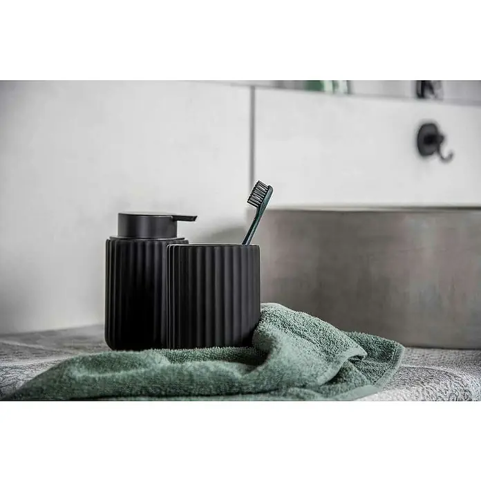 Wenko Belluno Seifenspender - Keramik, Schwarz - Elegantes Badezimmer-Set in Schwarz mit geriffelter Seifenspender und Zahnputzbecher, ergänzt durch ein weiches, grünes Handtuch.