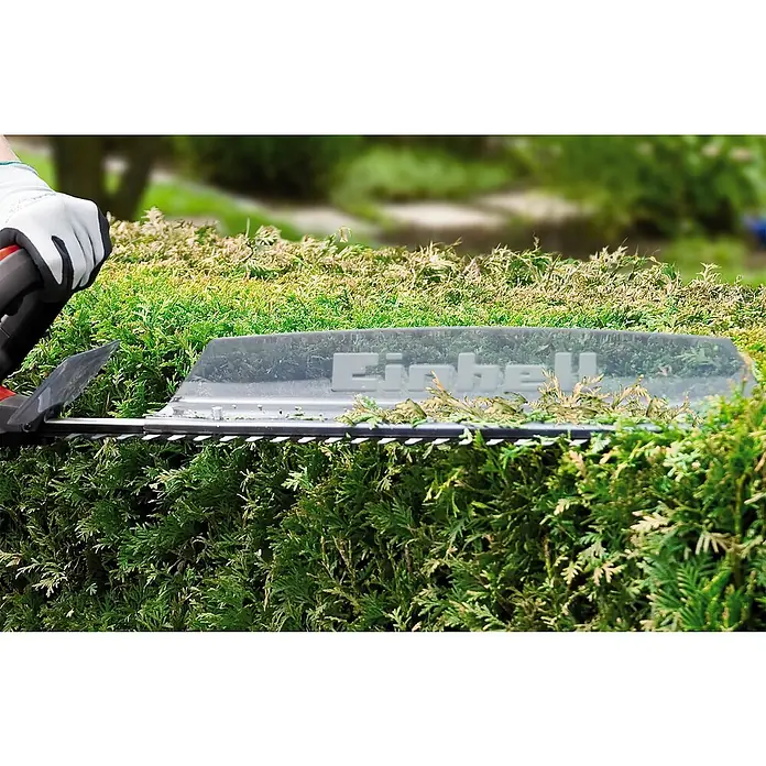 Einhell PXC 18V Cortasetos de batería GC-CH 1855/1 Li Kit - 18 V, Iones de litio, 1 batería, Longitud de corte: 55 cm - Primer plano de un cortasetos Einhell en acción, recortando con precisión un exuberante seto verde en un jardín, mostrando su eficiencia.