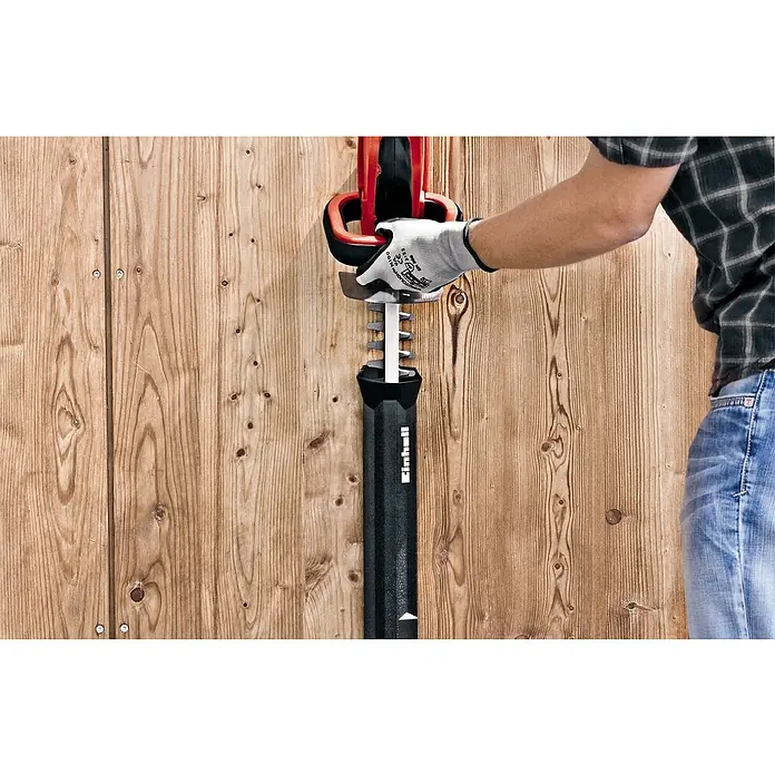 Einhell PXC 18V Cortasetos de batería GC-CH 1855/1 Li Kit - 18 V, Iones de litio, 1 batería, Longitud de corte: 55 cm - Una persona que sostiene un cortasetos Einhell con una cubierta protectora contra una pared de madera.