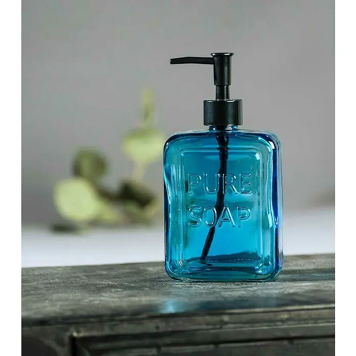 Wenko Seifenspender Pure SoapGlas, Blau - Ein blauer Seifenspender mit der Aufschrift "Pure Soap" und einem schwarzen Spenderkopf, stehend auf einer dunklen Oberfläche.