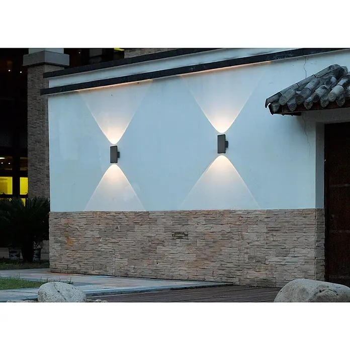 Trio Leuchten Außenwandleuchte Colorado - 3 W, L x B x H: 6,5 x 9 x 20 cm, Anthrazit, IP54 - Nahaufnahme von zwei Wandleuchten, die warmes Licht auf eine weiße Wand mit Steindekor strahlen und so eine gemütliche Atmosphäre schaffen.