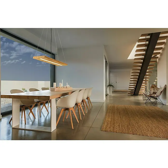 Trio Leuchten Brad LED-Pendelleuchte - 27 W, L x B x H: 20 x 100 x 150 cm, Holz, Warmweiß - Einrichtung mit langem Holztisch, Stühlen und einer hölzernen Hängelampe. Moderne Treppe und Teppich im Hintergrund. Elegantes Design.